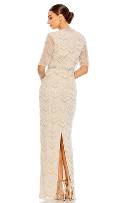 Woman wearing the Mac Duggal Beaded Fringe Long Formal Dress 94071—full-length, nude, with beaded details and short sleeves, features a back slit. She pairs it with metallic heels and is facing away from the camera.