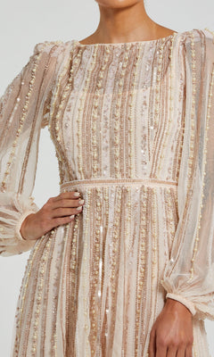 A person wearing the Mac Duggal 94081 long sleeve beige formal dress, featuring vertical stripes of sequins and beads, poses with one hand on their hip.