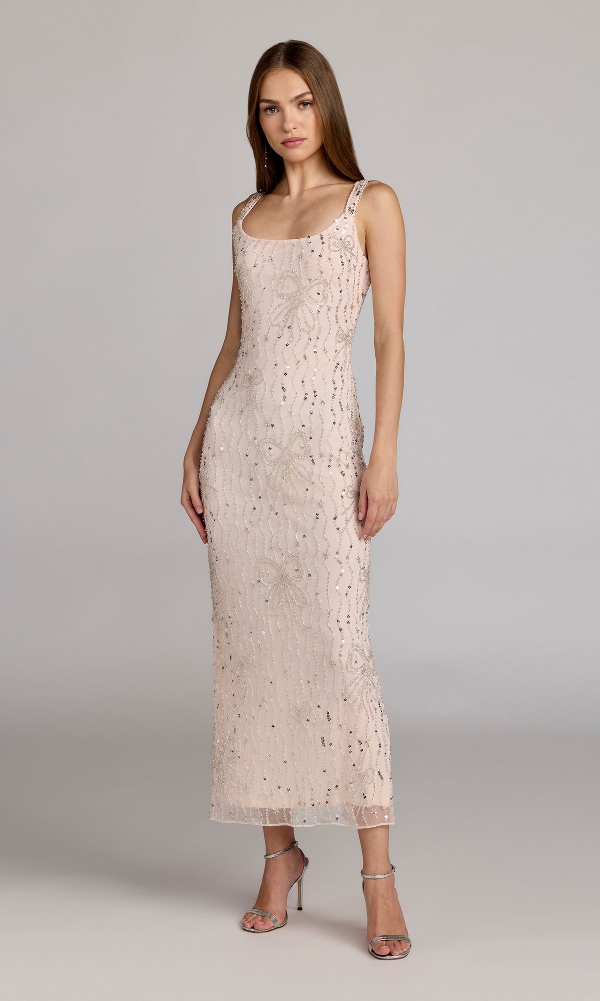 A woman poses in the Mac Duggal 94129 Long Formal Dress in blush, a sleeveless beaded mesh ankle-length gown with sequin embellishments, paired with silver heels, set against a plain gray background.