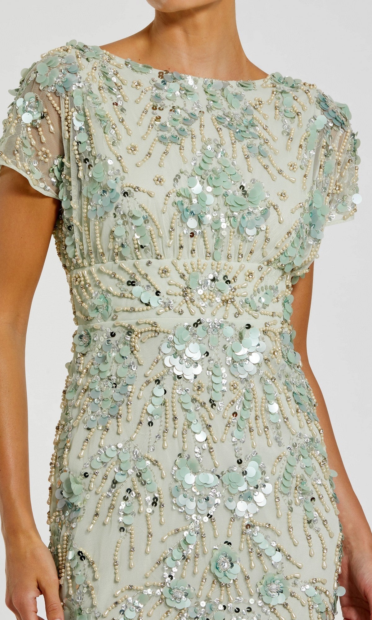A woman wears the Mac Duggal 94150 Midi Sequin Wedding Guest Dress, featuring short sleeves in cream with light green floral appliqués, sequins, and bead embellishments.