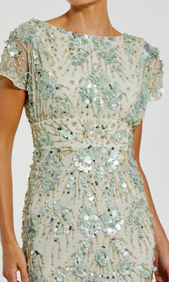 A woman wears the Mac Duggal 94150 Midi Sequin Wedding Guest Dress, featuring short sleeves in cream with light green floral appliqués, sequins, and bead embellishments.