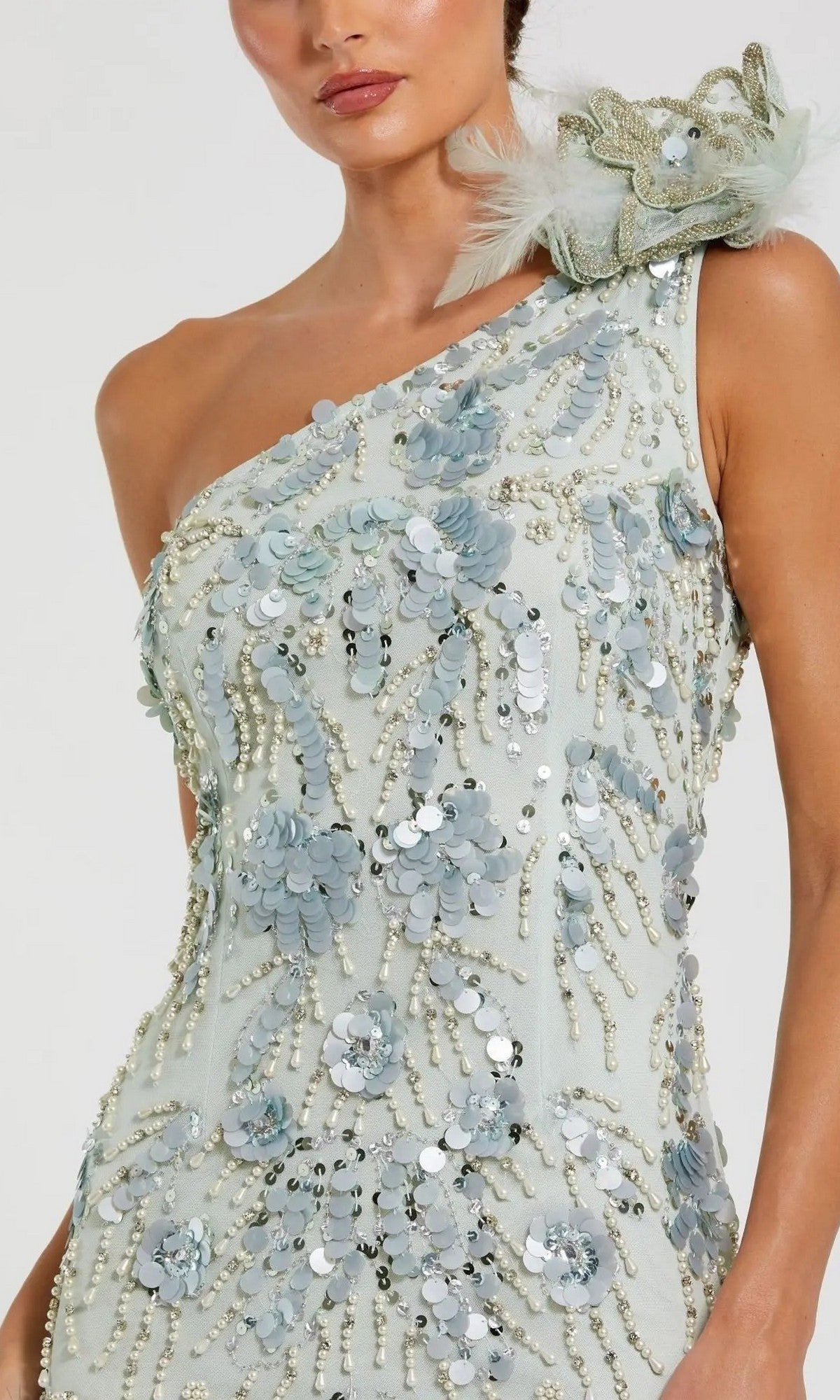 Wearing the Long Formal Dress: Mac Duggal 94151, a woman is dressed in a light blue, one-shoulder gown embellished with sequin beaded detailing, pearl-like beads, and featuring a large floral applique accented with feathers on the shoulder.