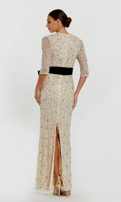 Woman in a floor-length, beaded oyster white Mac Duggal 94166 formal gown with three-quarter sleeves and a black belt, wearing high heels and standing with her back to the camera.