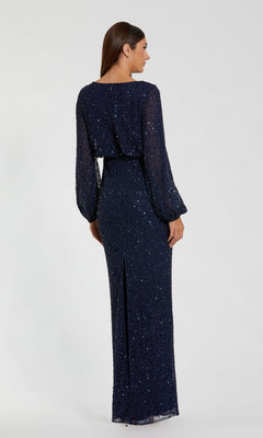 A woman is pictured standing and facing away from the camera against a plain background, wearing the Mac Duggal 94203 long formal dress. This navy blue gown features long sleeves, shimmering sequins, a belted waist, and a back slit. Its modest design creates an elegant silhouette ideal for sophisticated occasions.