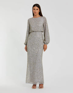 A woman stands in a full-length, long-sleeve platinum gold gown—Mac Duggal 94203—with a cinched waist and open-toe heels, set against a plain white background. This elegant sequin dress from Mac Duggal exudes both glamour and the sophistication of a modest long formal dress.