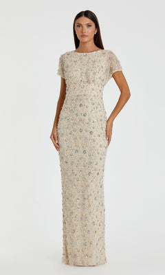 A woman wears the Mac Duggal 94205 Embellished Long Formal Dress—floor-length, short-sleeved, beige, and covered in silver sequins—standing against a plain white background.