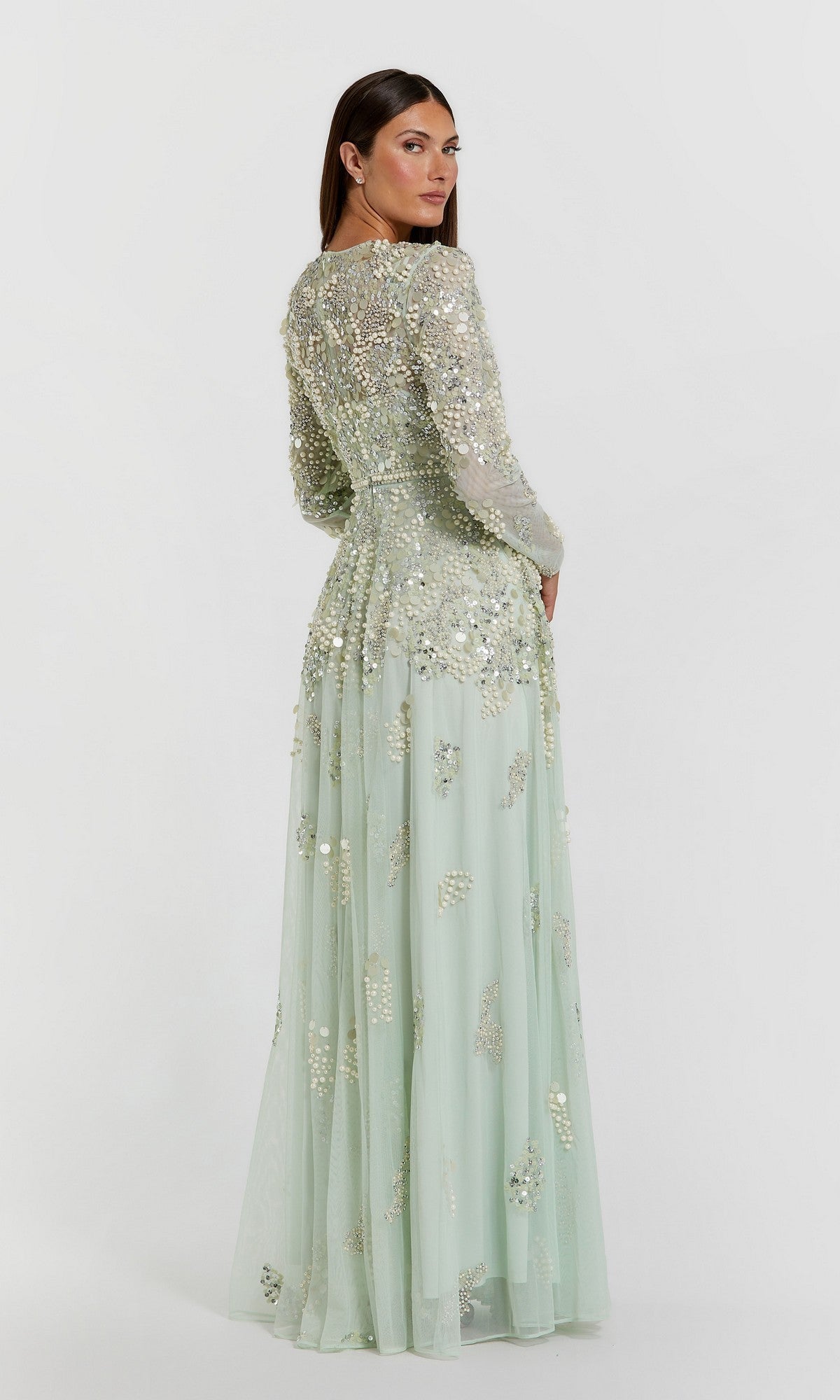 A woman is shown standing with her back to the camera against a plain white background, wearing the Mac Duggal 94215 long formal dress—a pale green, floor-length evening gown adorned with silver sequin and bead embellishments.