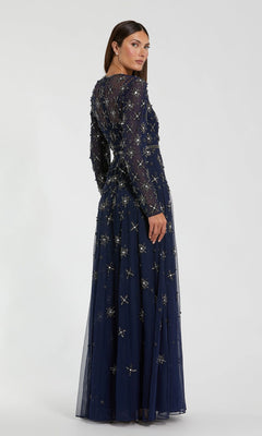 A woman stands facing away against a plain background, wearing the Mac Duggal 94216 long formal dress—a navy gown with long sleeves and intricate beaded embellishments.
