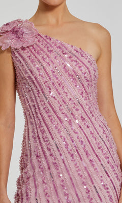 Person wearing the Mac Duggal 94221 Long Formal Dress in light pink, featuring sequin and bead detailing, a large fabric flower on one shoulder, and elegant diagonal accents.