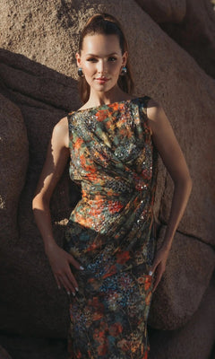 A woman stands before large rock formations, looking at the camera in a sleeveless Mac Duggal 94263 long formal dress featuring floral mesh and sequin accents.