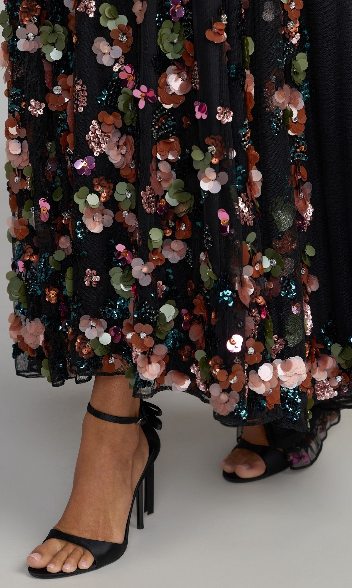 Wearing the Mac Duggal 94270 long formal dress, adorned with colorful 3D sequin flowers, and paired with black high-heeled sandals, a person creates a striking and eye-catching look.