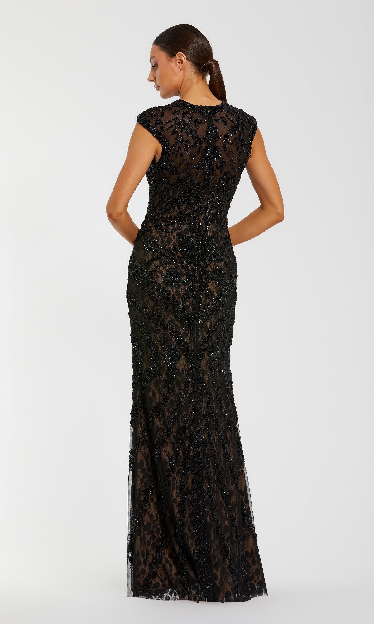 A woman stands facing away, wearing the Sequin Long Black Formal Dress: Mac Duggal 94276, a floor-length gown with cap sleeves and sequin detailing.