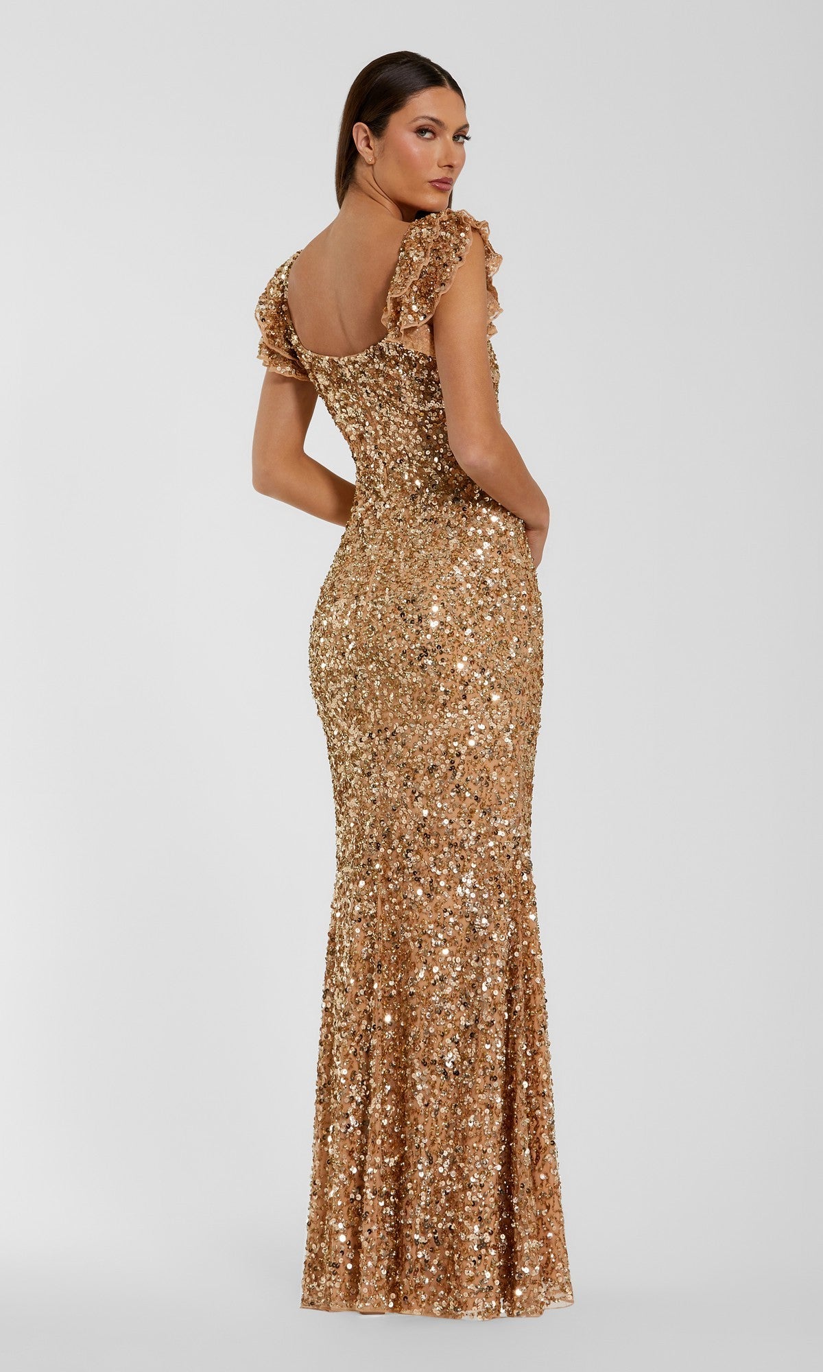 A woman poses facing away and looking over her shoulder, showcasing the Long Formal Dress: Mac Duggal 94279—a floor-length gold sequin gown with short ruffled sleeves—against a plain light background.