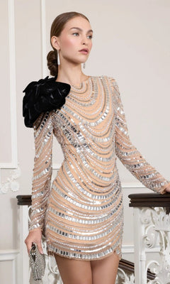 Woman wearing the Mac Duggal 94284 short party dress in Silver Nude, featuring sparkling sequins and silver patterns with a statement black flower on the shoulder. She holds a small clutch and stands beside a decorative white railing.