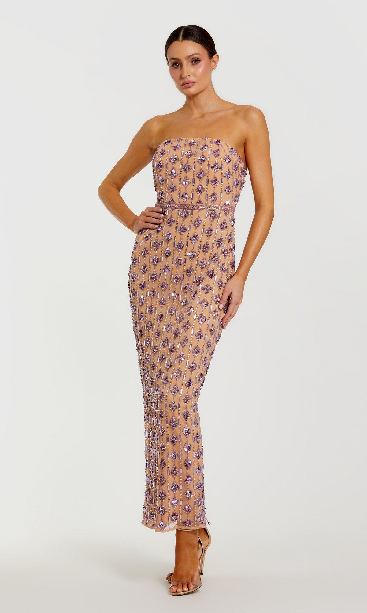 A woman poses with one hand on her hip against a plain white background, modeling the Mac Duggal 94293 long formal dress—a strapless gown in floor-length nude lilac, adorned with glamorous purple sequin embellishments.