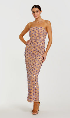 A woman poses with one hand on her hip against a plain white background, modeling the Mac Duggal 94293 long formal dress—a strapless gown in floor-length nude lilac, adorned with glamorous purple sequin embellishments.