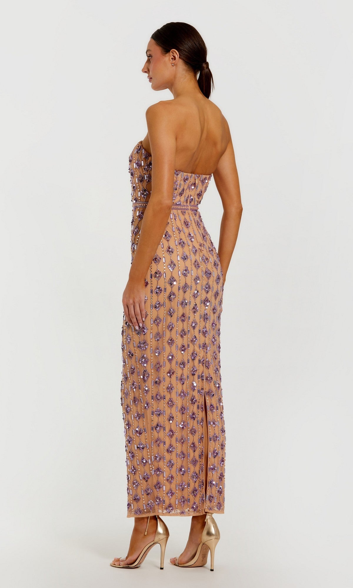 A woman is seen from the back, against a plain light background, wearing the Long Formal Dress: Mac Duggal 94293—a strapless, floor-length peach gown embellished with purple beadwork and sequins—paired with high-heeled sandals.