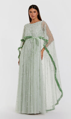 A woman wearing the Mac Duggal 94294 long formal dress in jade—a floor-length gown featuring a sheer, embellished overlay, pleated skirt, and green ribbon details—stands against a plain white background. The look captures effortless elegance, reminiscent of a crystal beaded design.