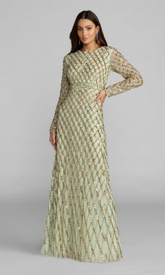 A woman stands against a plain gray background wearing the Mac Duggal 94318 Long Formal Dress in sage, featuring modest long sleeves, a full-length silhouette, and a diamond-patterned overlay adorned with sequin embellishments.