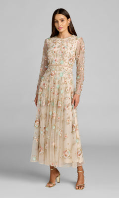 A woman stands against a plain gray background wearing the ankle-length Mac Duggal 94336 dress in Beige Multi, featuring sheer long sleeves and beaded floral embellishments, paired with gold heels.