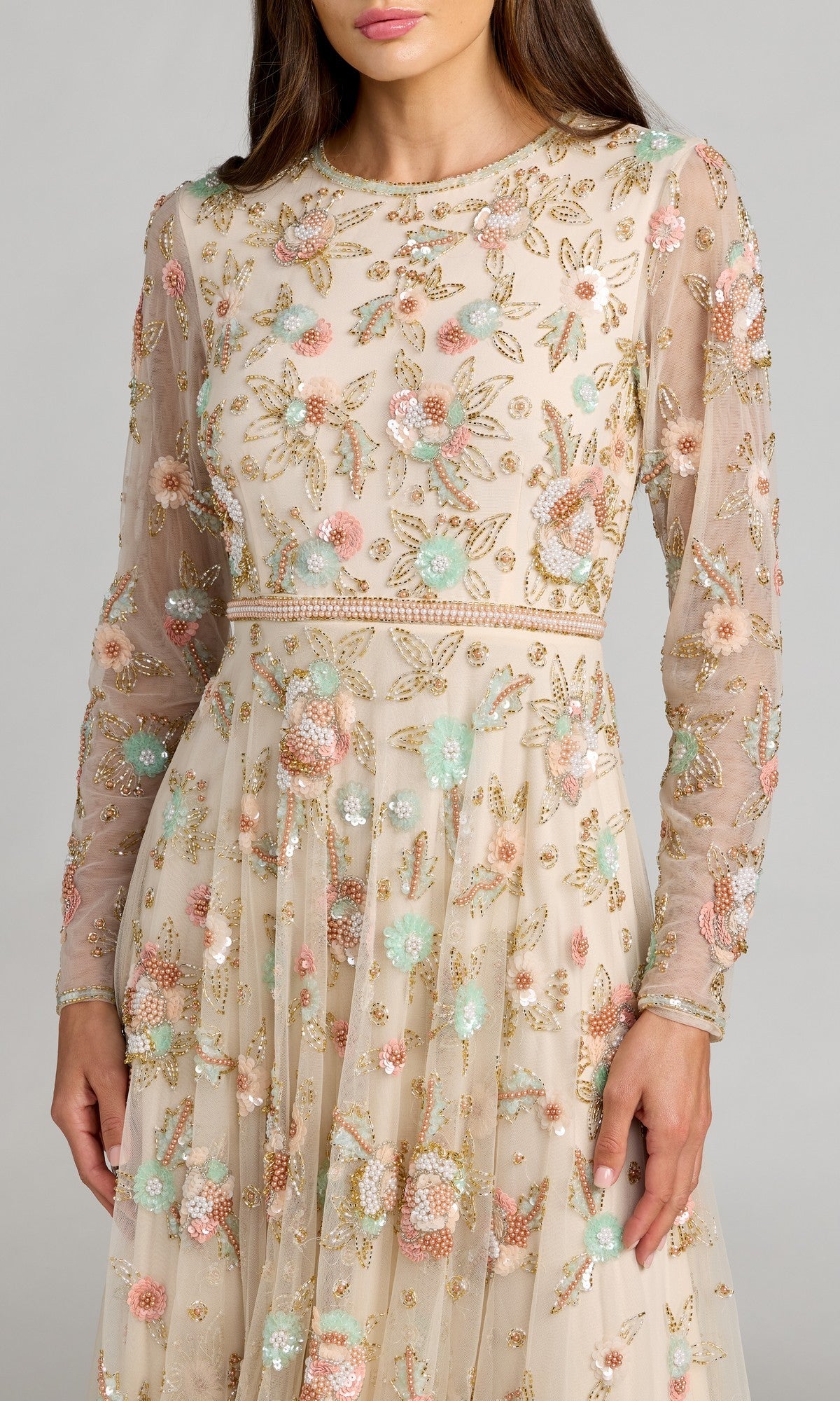 A woman wearing the Mac Duggal 94336 ankle-length floral dress, designed with an A-line silhouette, sheer long sleeves, and colorful beaded floral embellishments and embroidery, shown from chest to knees.