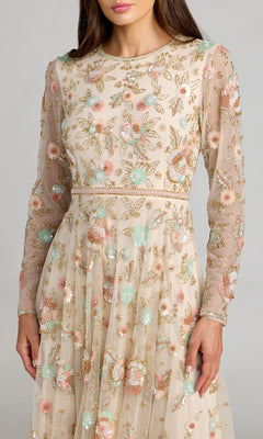 A woman wearing the Mac Duggal 94336 ankle-length floral dress, designed with an A-line silhouette, sheer long sleeves, and colorful beaded floral embellishments and embroidery, shown from chest to knees.