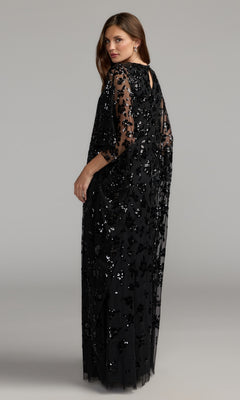 A woman stands against a plain gray background, looking over her shoulder in the Mac Duggal 9441 Cape-Sleeve Long Formal Dress—a modest evening gown featuring black sequin embellishments and sheer cape sleeves.