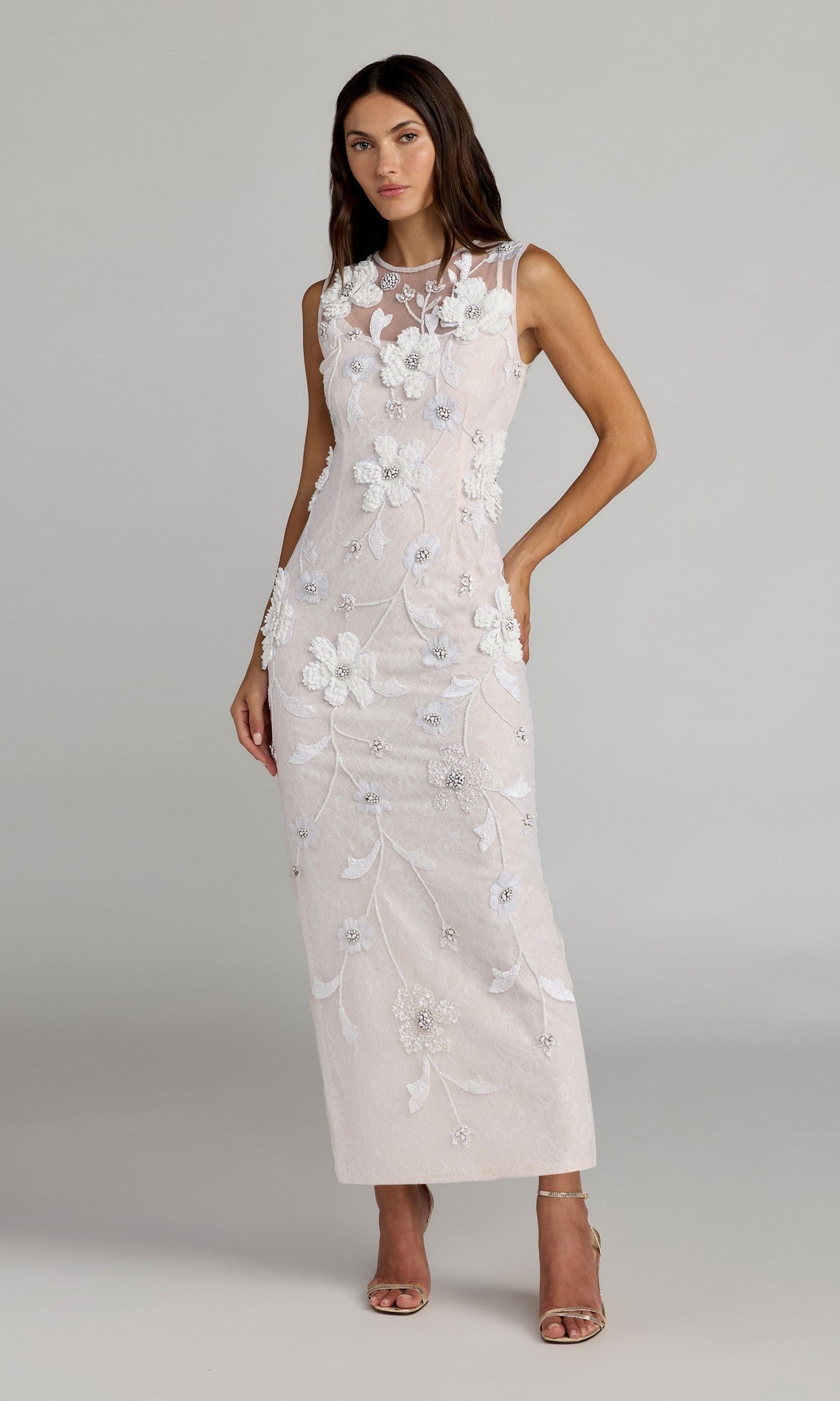 A woman stands against a plain background in the ivory Long Formal Dress: Mac Duggal 9465, a sleeveless, floor-length gown featuring floral embroidery, paired with open-toed heels.
