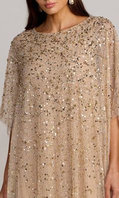 A woman is shown from shoulders to midsection wearing the Mac Duggal 9475 Long Formal Dress, a sheer, light beige gown embellished with gold and silver sequins and beadwork, paired with large earrings.