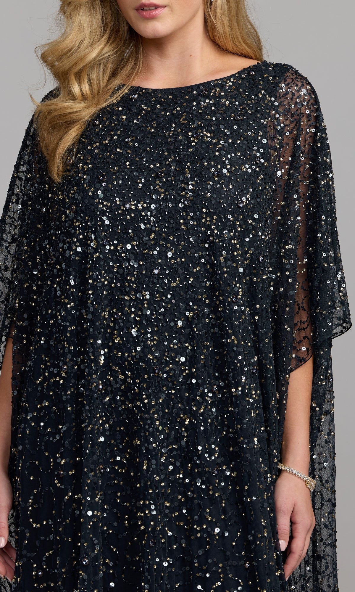A woman wearing the Mac Duggal 9475 long formal dress, featuring dark sequin beading, short sleeves, and sheer detailing, stands against a plain background.