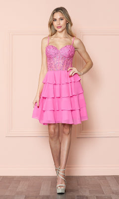 A woman stands against a peach wall, wearing the Poly USA 9494 Short Ruffled Lace-Up Hoco Dress featuring a corset-style lace bodice, sheer panels, and tiered mini skirt, styled with silver high-heeled sandals.