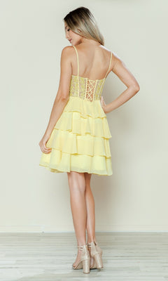 Woman stands on a wooden floor, facing away, wearing the Short Ruffled Lace-Up Hoco Dress: Poly USA 9494—a yellow, tiered, sleeveless dress with corset-style bodice, lace-up back details—and strappy block-heeled sandals.