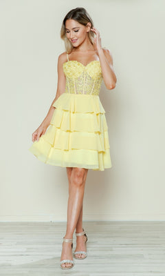 Woman wearing the Short Ruffled Lace-Up Hoco Dress (Poly USA 9494)—an affordable yellow, tiered mini dress with a corset-style bodice and spaghetti straps—standing indoors on a light wood floor.