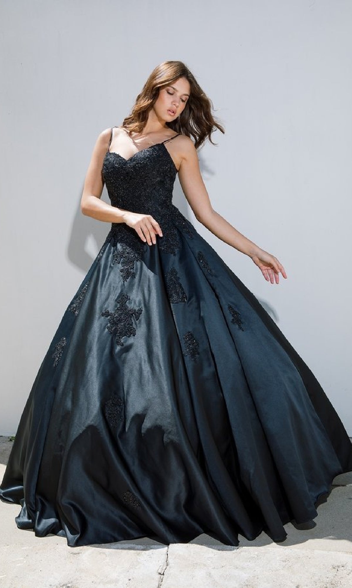 A woman poses against a plain, light-colored wall in the Classic Long Prom Ball Gown: Eureka 9500, featuring black lace detailing and a chic lace-up back.