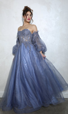 Someone stands against a light wall wearing the Eureka 9505G, a strapless, floor-length prom ball gown with long sheer puffy sleeves and intricate embellishments in lavender.