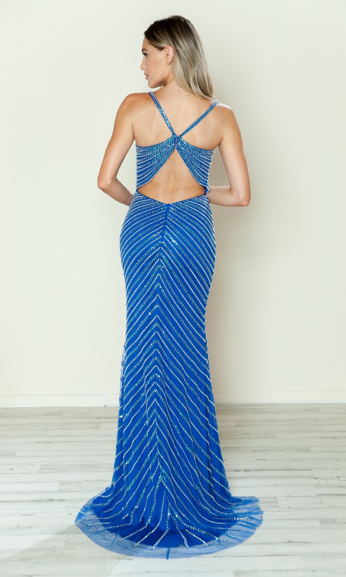 A woman faces away, wearing the Cut-Out Long Beaded Prom Dress (Poly USA 9530)—a fitted, floor-length blue gown featuring silver stripes, crisscross straps, and a stylish back cutout.