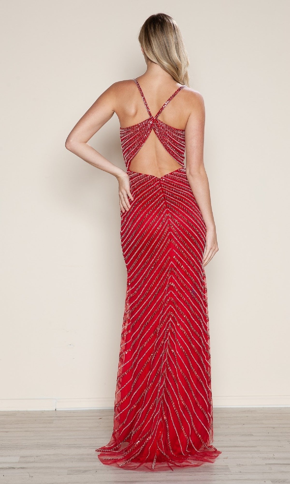A woman faces away wearing the Cut-Out Long Beaded Prom Dress: Poly USA 9530, featuring diagonal stripes, crisscross straps, and an open back against a plain background.
