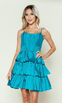 A person models the Short Homecoming Dress: Poly USA 9590, a sleeveless fit-and-flare dress with a teal, tiered A-line skirt, standing against a plain light background facing the camera with one hand on their hip.