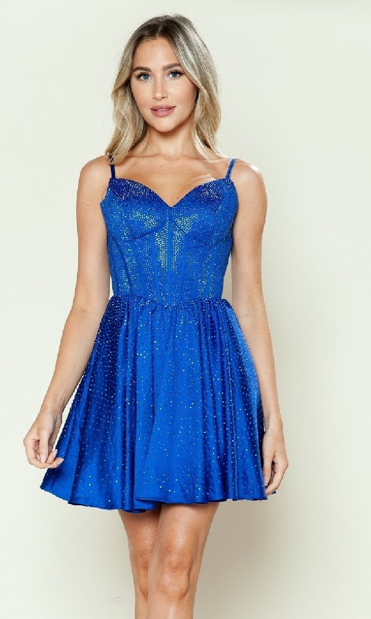 A woman wears the Sparkly Homecoming Dress with Pockets: Poly USA 9594, a blue sleeveless spaghetti strap short dress with a fitted bodice and flared skirt, standing against a plain light background.