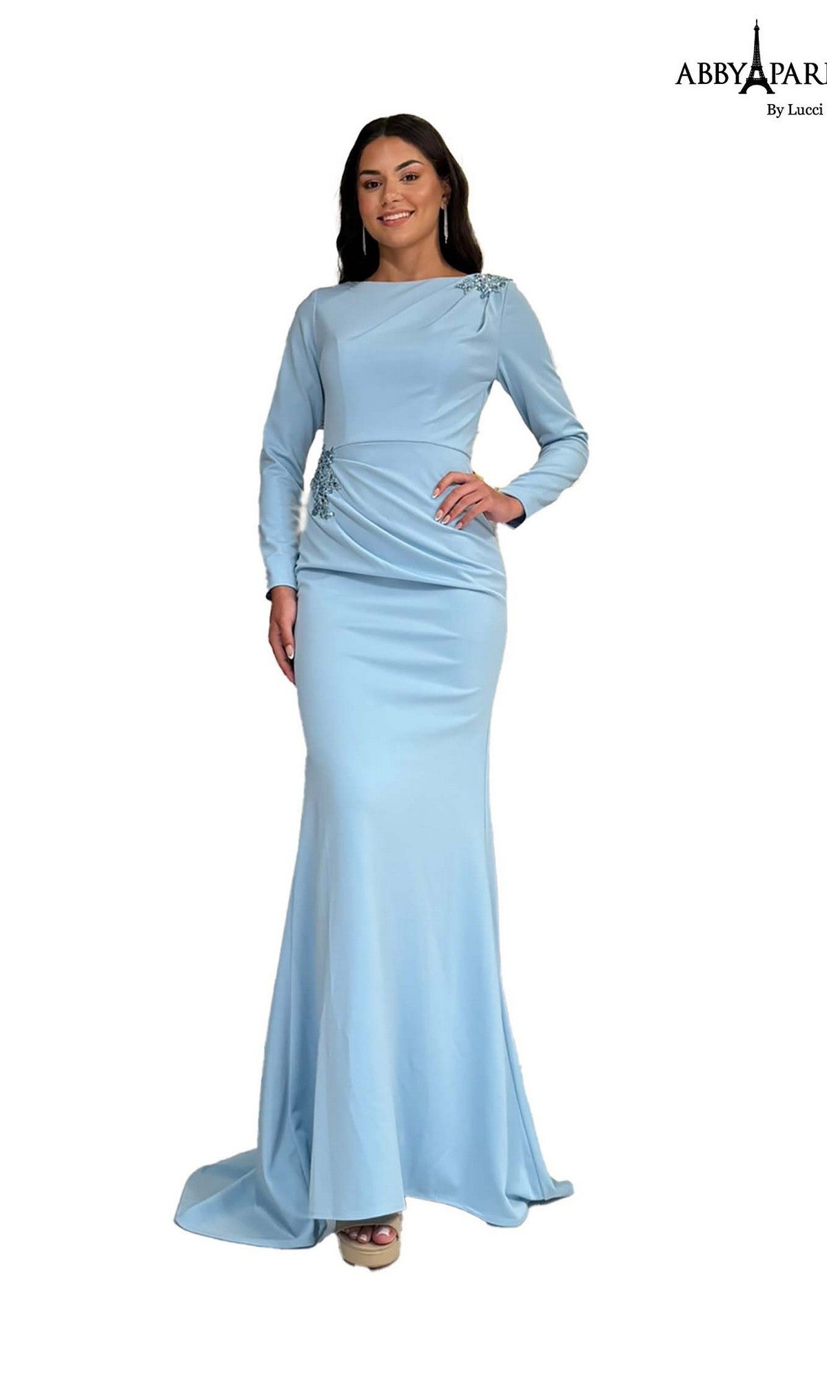 A woman stands and smiles against a white background, wearing the Abby Paris 96090 long formal dress in dusty blue with long sleeves and subtle embellishments.