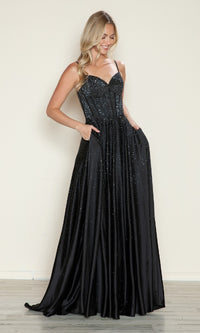 A woman stands against a plain background wearing the Poly USA 9610, a long black strapless prom dress with a corset bodice and pockets.