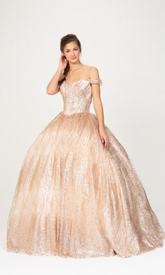 A woman is wearing the Quinceanera Dress 9616 by Eureka, an off-the-shoulder, champagne-colored ball gown with a full, shimmery skirt, posing gracefully against a plain white background.