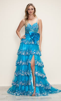 A woman wears the Poly USA 9626 long prom dress, featuring an A-line silhouette, tiered blue skirt with floral details, a large waist bow, and thigh-high slit, standing against a plain light background.