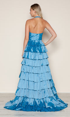A woman stands with her back to the camera in the Poly USA 9642 Ruffled Long Halter Prom Dress, featuring blue tiered ruffles and a dramatic floor-length train.