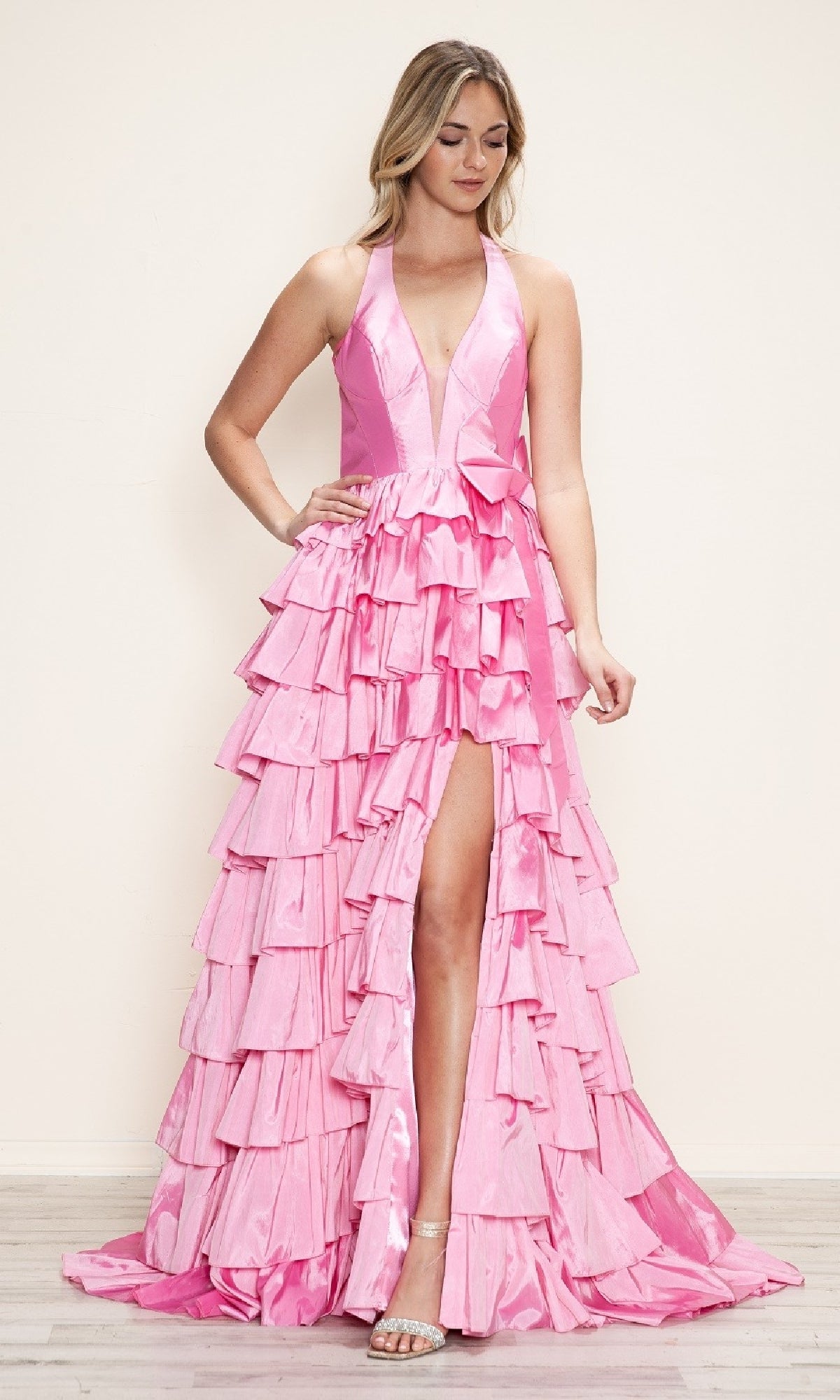 A woman stands on a light-colored floor against a plain background, wearing the Poly USA 9642 Ruffled Long Halter Prom Dress in pink with a deep v-neck, ruffles, and a high slit.
