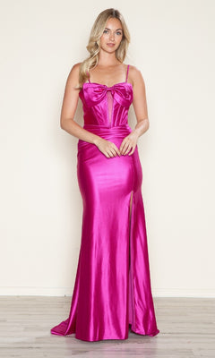 A woman stands against a plain light wall in the Front-Bow Long Cut-Out Prom Dress: Poly USA 9644— a shiny hot pink, floor-length gown featuring spaghetti straps, a front slit, and a bow detail on the bodice.