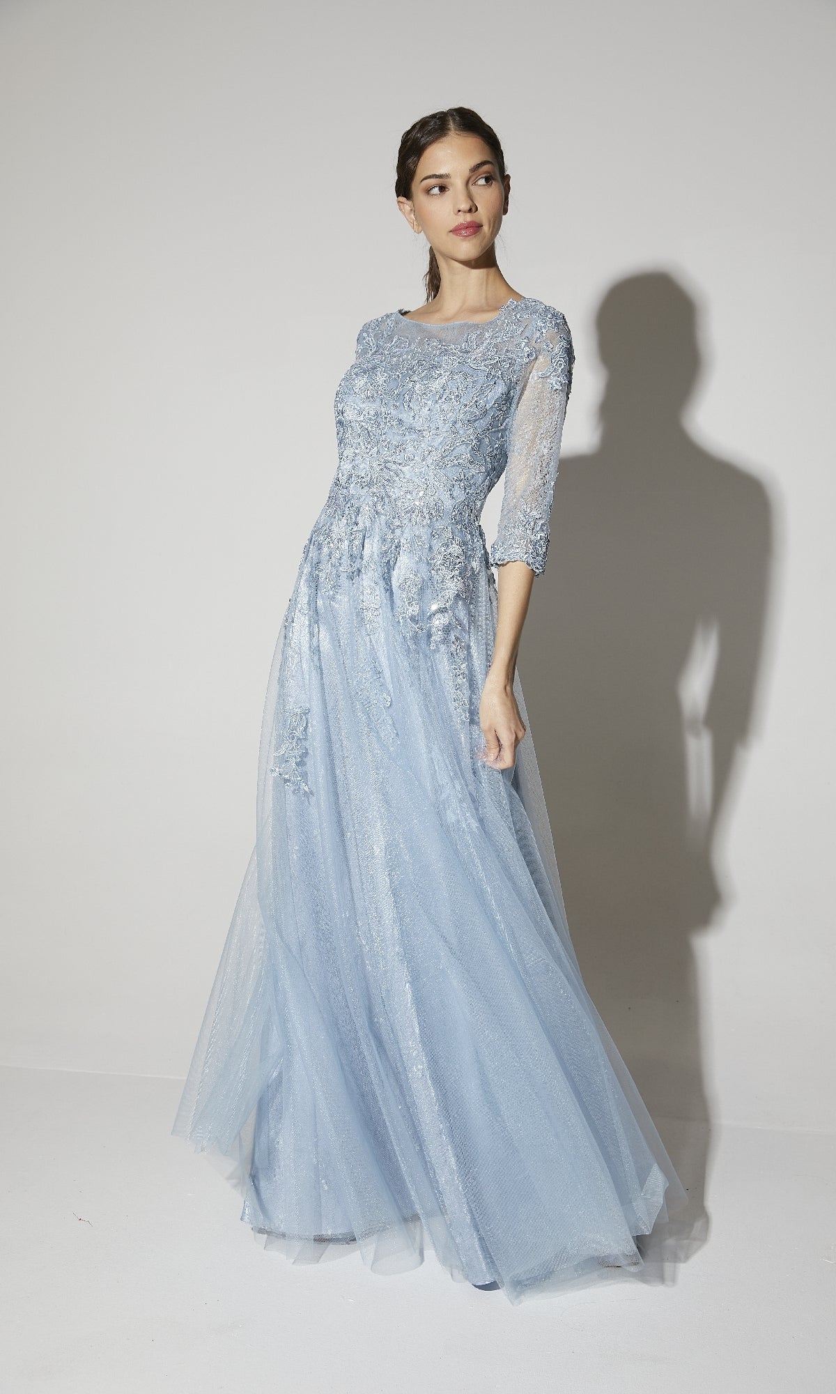 Woman wearing the Eureka 9660 Flowy Long Sleeve Long Formal Dress in light blue with a lace bodice and sheer sleeves, standing against a plain white background.