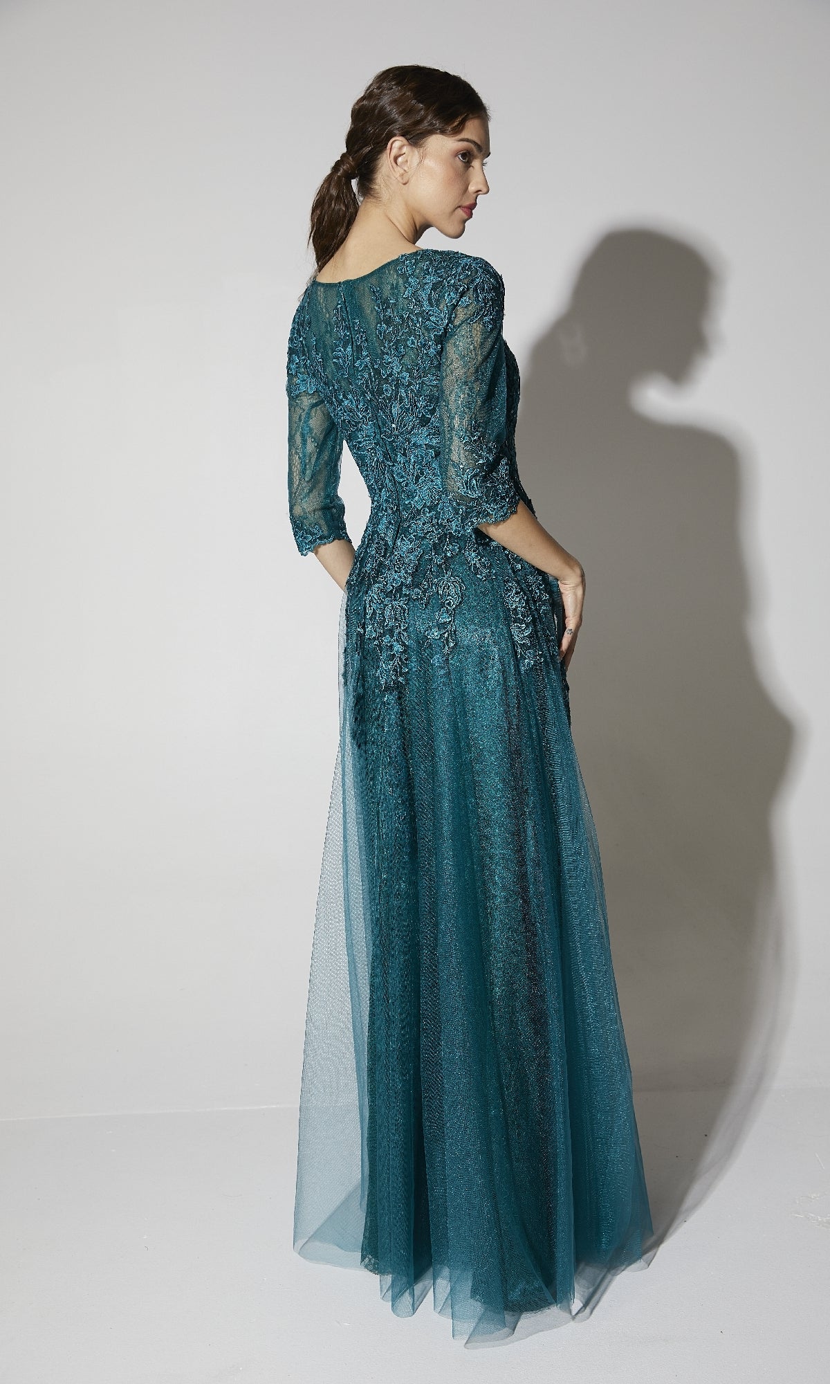 A woman in the Eureka 9660 Flowy Long Sleeve Long Formal Dress stands facing away, glancing over her shoulder against a plain light background.