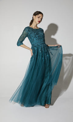 Woman wearing the Flowy Long Sleeve Long Formal Dress: Eureka 9660, showcasing a teal lace bodice, three-quarter sleeves, and a flowing tulle skirt against a plain white background.