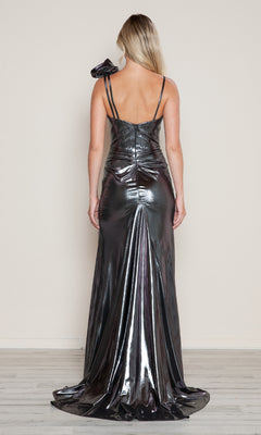A woman faces away, wearing the Poly USA 9680 Ruffle Shoulder Metallic Prom Gown—a shiny silver evening dress with thin straps and a ruffled bow detail on one shoulder.
